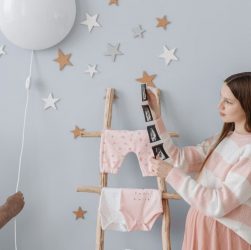 Expectant mother holding ultrasound images in a beautifully decorated nursery with whimsical elements.