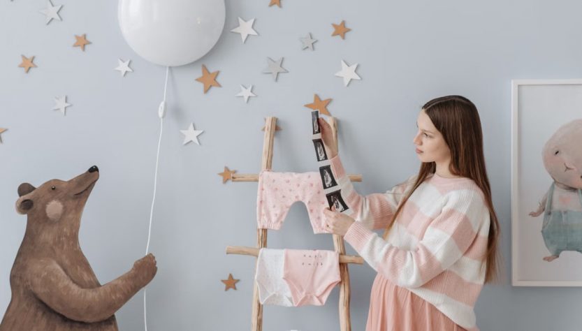 Expectant mother holding ultrasound images in a beautifully decorated nursery with whimsical elements.